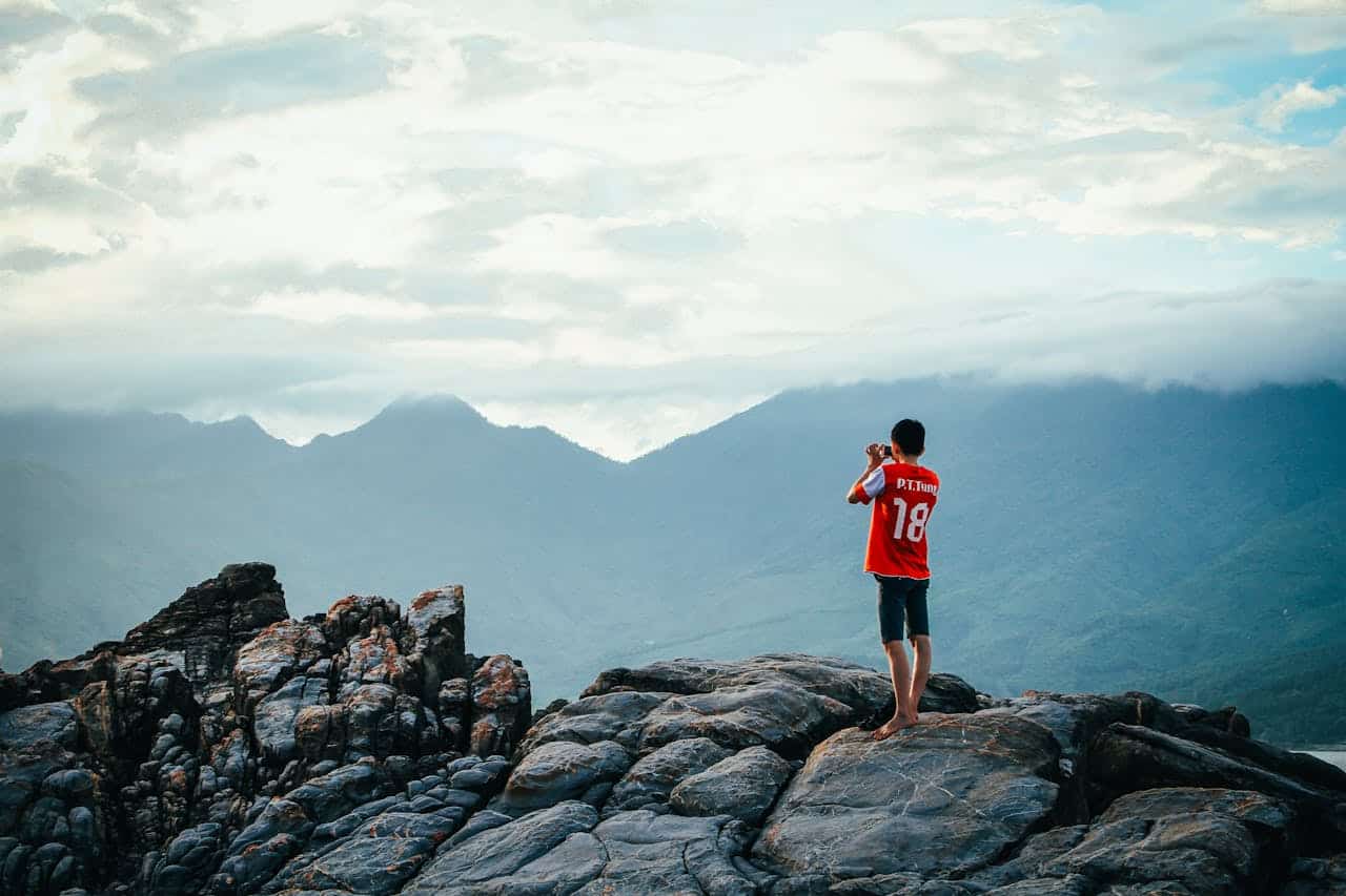 about-03 A person enjoying a scenic view on a rocky mountain peak, surrounded by lush landscapes and wide skies.